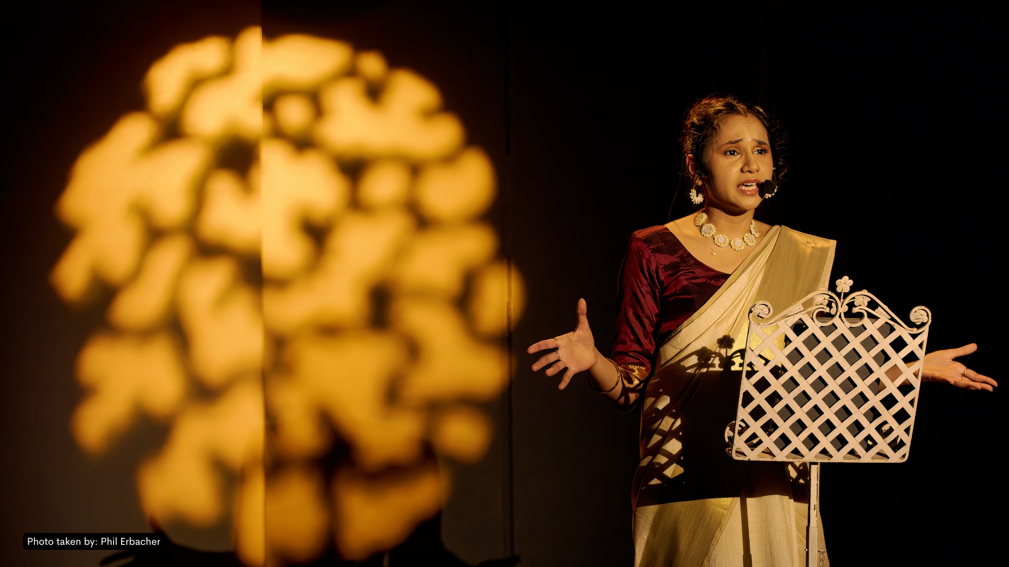 Production photo from And What Will People Say? — Kersh in mid-Bharatanatyam pose under deep amber stage light, audience-close composition.